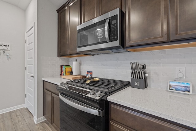 kitchen with tasteful backsplash, light stone counters, stainless steel appliances, dark brown cabinets, and light wood-style floors