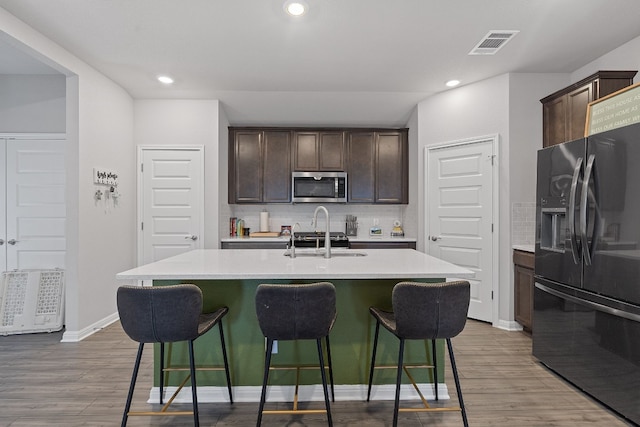 kitchen with a breakfast bar area, stainless steel microwave, visible vents, a sink, and black fridge