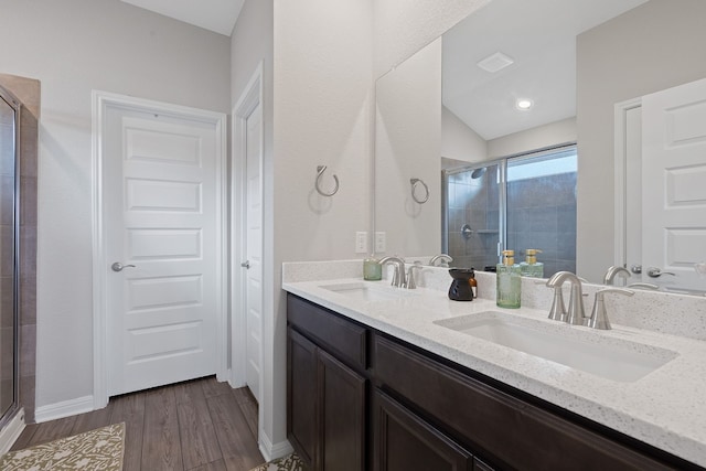 full bath featuring double vanity, a sink, a shower stall, and wood finished floors