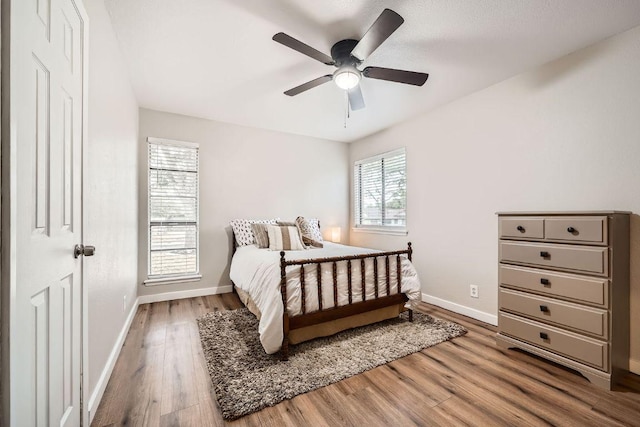 bedroom with a ceiling fan, multiple windows, baseboards, and wood finished floors