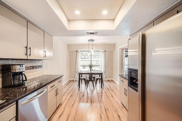 kitchen featuring stainless steel appliances, visible vents, light wood-style floors, decorative backsplash, and a raised ceiling