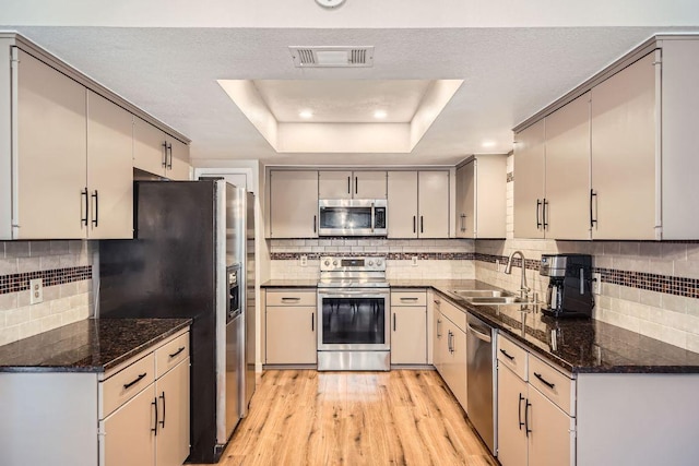 kitchen with stainless steel appliances, a sink, visible vents, light wood finished floors, and a raised ceiling