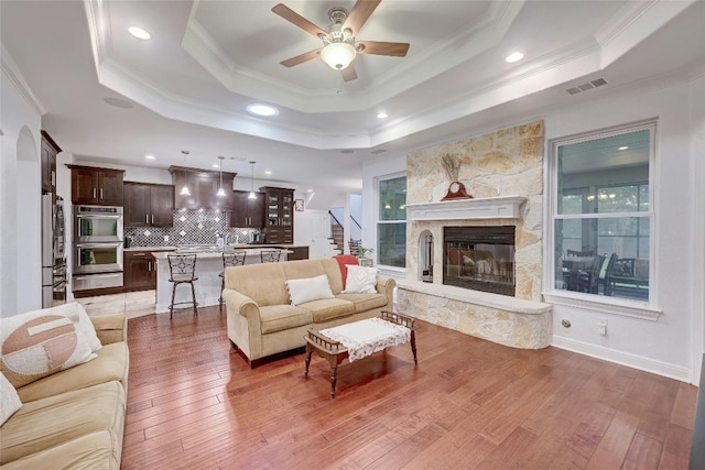 living room with a raised ceiling, visible vents, ornamental molding, ceiling fan, and light wood-type flooring