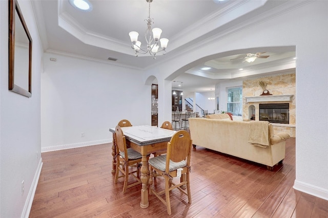 dining space featuring ornamental molding, arched walkways, a raised ceiling, and hardwood / wood-style flooring