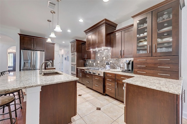 kitchen featuring arched walkways, tasteful backsplash, visible vents, appliances with stainless steel finishes, and a sink