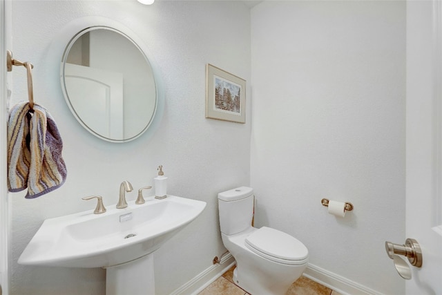 half bathroom with toilet, tile patterned flooring, baseboards, and a sink