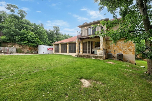 rear view of house with a yard, a sunroom, central AC, a garage, and stone siding