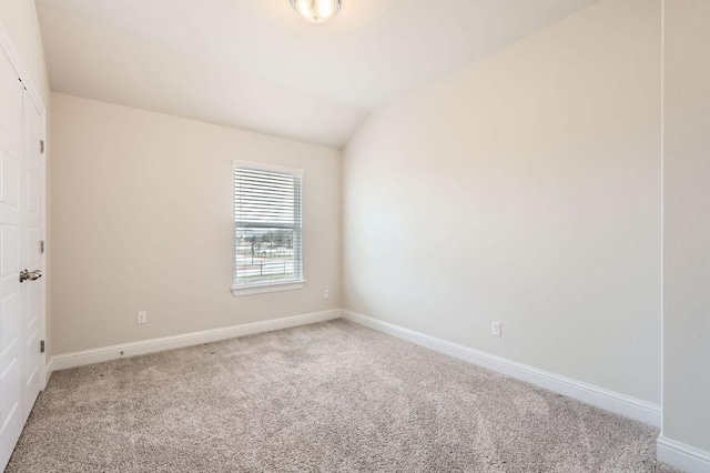 empty room featuring lofted ceiling, carpet flooring, and baseboards