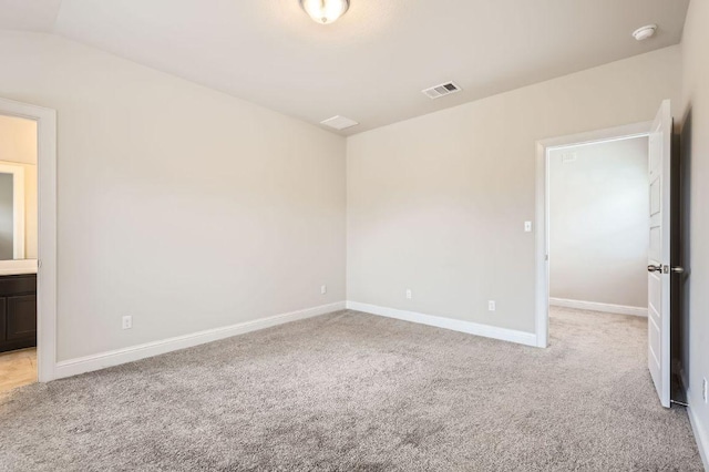 spare room featuring baseboards, lofted ceiling, visible vents, and light colored carpet