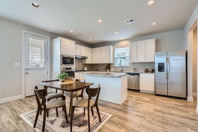 kitchen featuring visible vents, decorative backsplash, a kitchen island, stainless steel appliances, and under cabinet range hood