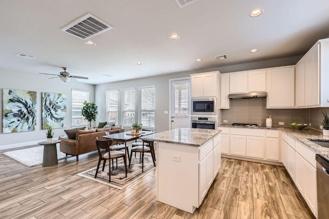 kitchen with stainless steel appliances, visible vents, under cabinet range hood, and tasteful backsplash