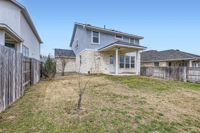 back of property featuring stone siding, a fenced backyard, a lawn, and a patio