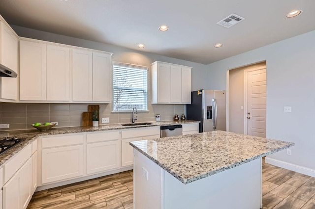 kitchen featuring stainless steel appliances, a sink, visible vents, decorative backsplash, and light wood finished floors