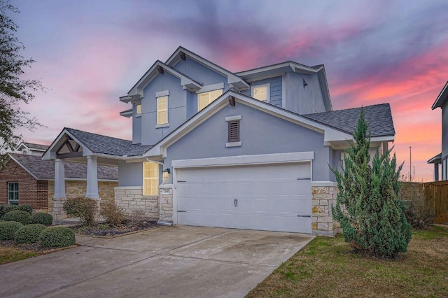 view of front of property featuring a shingled roof, concrete driveway, stone siding, fence, and stucco siding