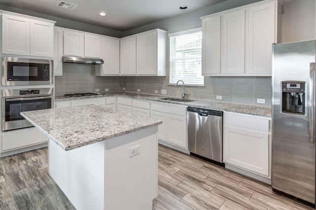 kitchen with under cabinet range hood, a sink, white cabinetry, appliances with stainless steel finishes, and a center island