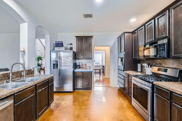 2141 Dragon Trl, New Braunfels, TX 78130 - kitchen with stainless steel appliances, tasteful backsplash, arched walkways, dark brown cabinets, and finished concrete floors