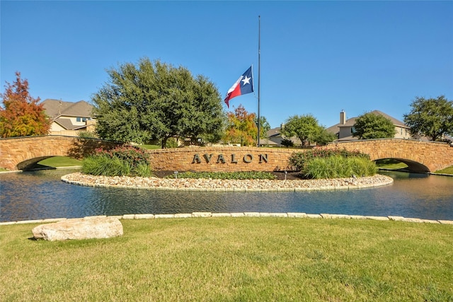 community / neighborhood sign featuring a water view and a yard