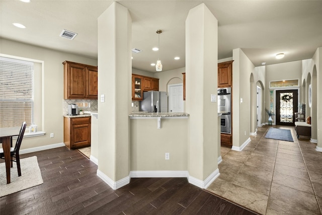 kitchen with brown cabinets, appliances with stainless steel finishes, arched walkways, and decorative backsplash