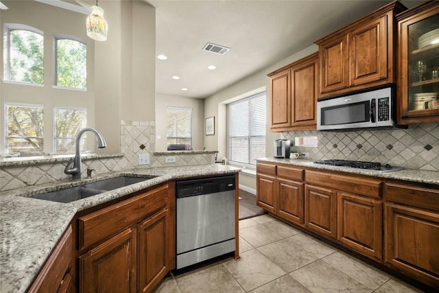 kitchen featuring visible vents, light stone counters, brown cabinets, stainless steel appliances, and a sink