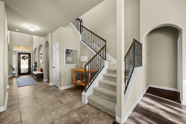 foyer entrance featuring stairway, arched walkways, a towering ceiling, and baseboards