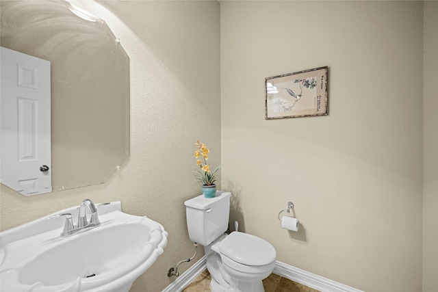 half bathroom featuring toilet, baseboards, a sink, and tile patterned floors