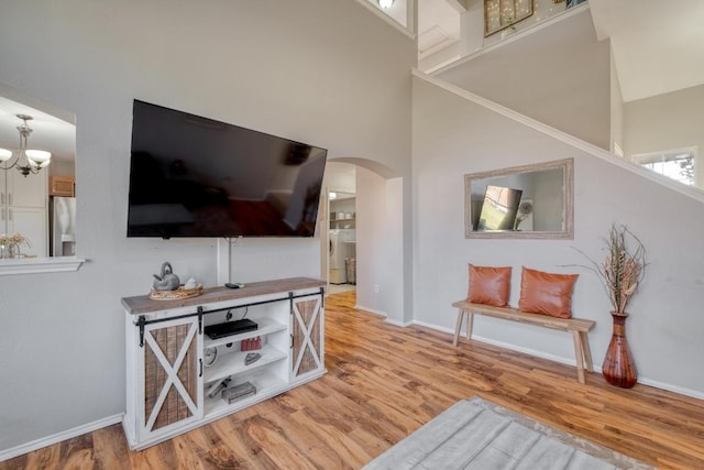 living room featuring arched walkways, a chandelier, a towering ceiling, baseboards, and light wood-style floors