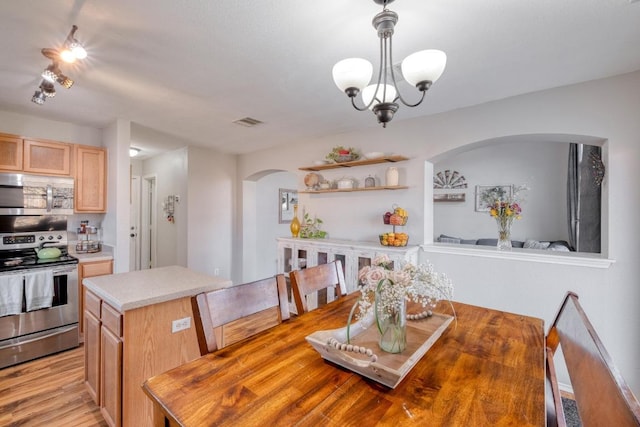 dining space featuring arched walkways, light wood-type flooring, visible vents, and an inviting chandelier