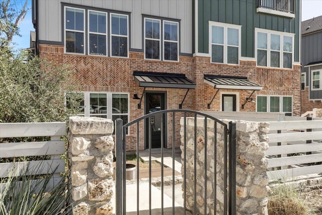 view of front facade featuring a standing seam roof, a fenced front yard, board and batten siding, and brick siding