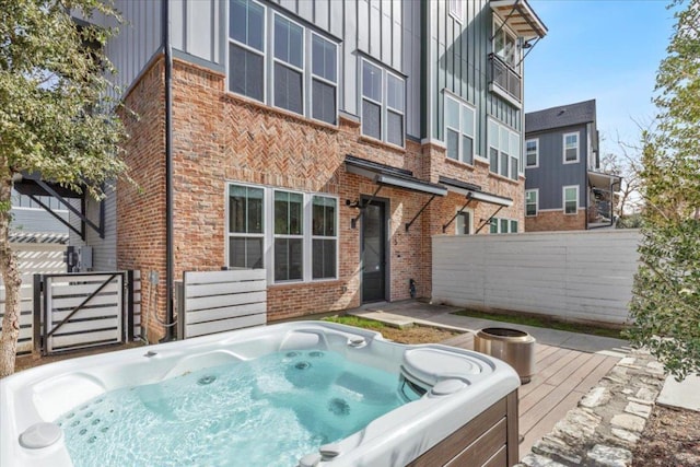 back of property with board and batten siding, brick siding, fence, and a hot tub