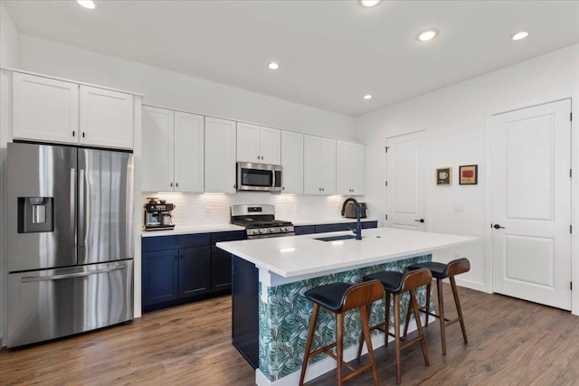 kitchen featuring dark wood-style floors, appliances with stainless steel finishes, a sink, a kitchen bar, and backsplash