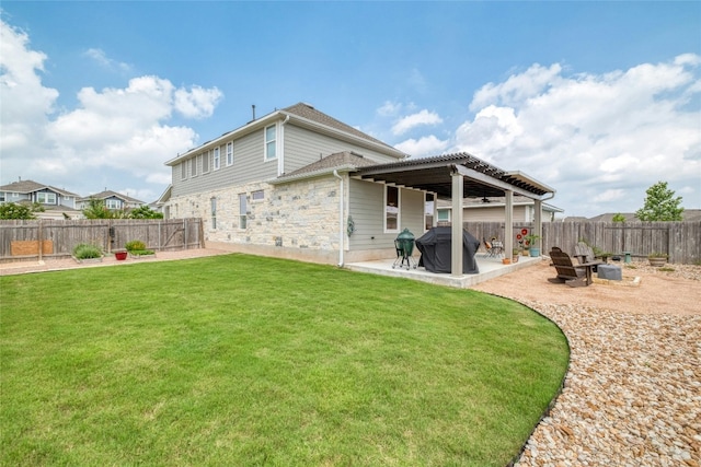 back of property with a fire pit, stone siding, a fenced backyard, a yard, and a patio area