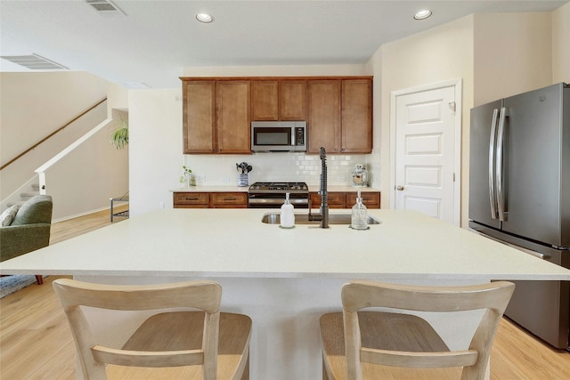 kitchen featuring appliances with stainless steel finishes, brown cabinetry, backsplash, and light wood-style flooring