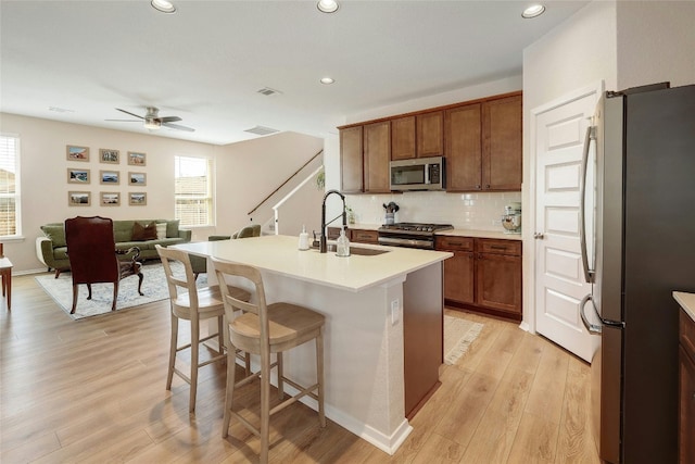 kitchen with a breakfast bar, decorative backsplash, appliances with stainless steel finishes, light wood-style floors, and a sink