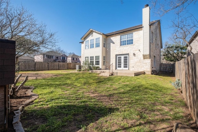 rear view of house featuring stone siding, french doors, a lawn, and a fenced backyard