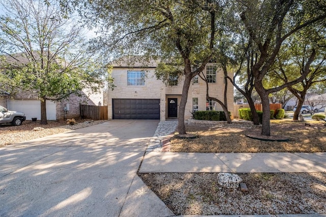 view of front of house featuring an attached garage, stone siding, concrete driveway, and fence