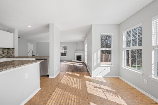 interior space featuring a glass covered fireplace, light tile patterned flooring, dishwasher, and backsplash