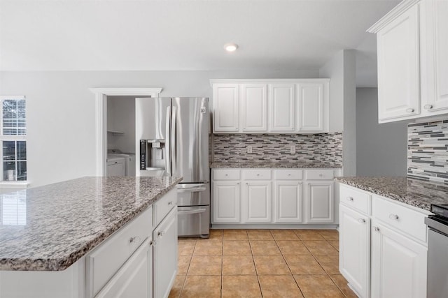 kitchen with stainless steel refrigerator with ice dispenser, tasteful backsplash, white cabinets, light tile patterned flooring, and washer and dryer