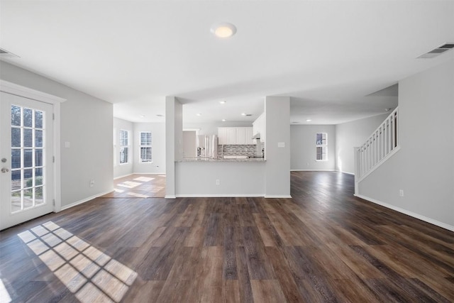 unfurnished living room featuring a healthy amount of sunlight, visible vents, and dark wood-type flooring