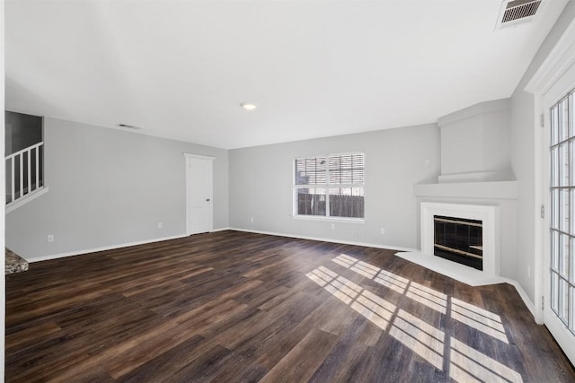 unfurnished living room featuring dark wood-style floors, stairway, visible vents, and a glass covered fireplace