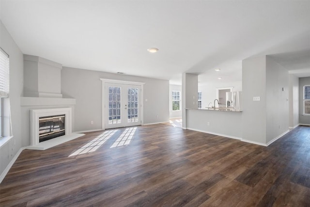 unfurnished living room with baseboards, dark wood finished floors, french doors, and a glass covered fireplace