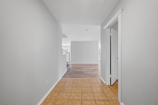 corridor with light tile patterned floors, stairs, and baseboards