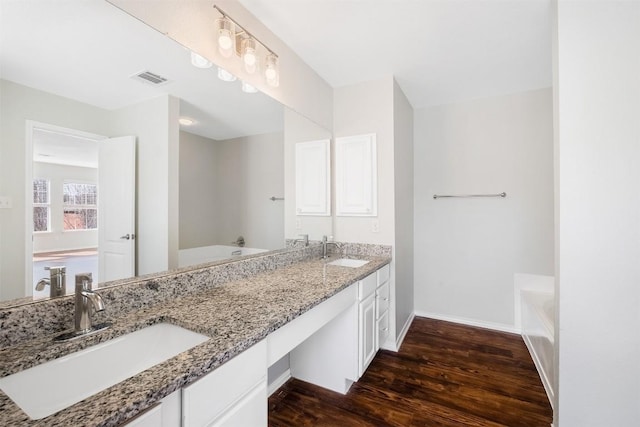 full bath with double vanity, a sink, a bath, and wood finished floors