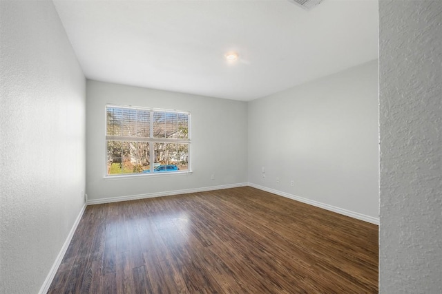 spare room featuring dark wood-type flooring, a textured wall, and baseboards