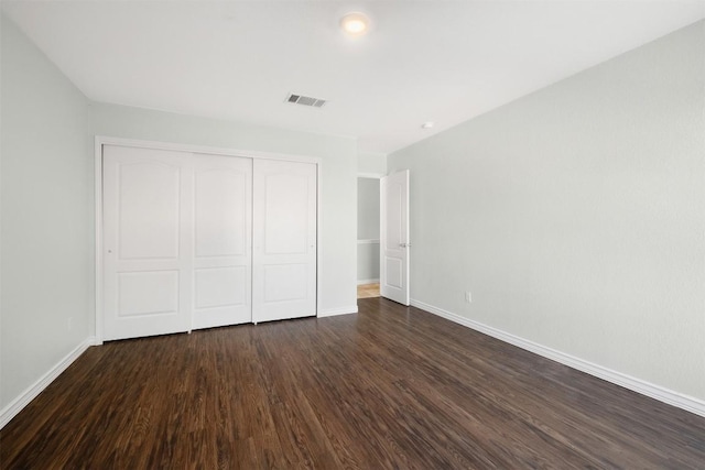 unfurnished bedroom featuring a closet, dark wood finished floors, visible vents, and baseboards