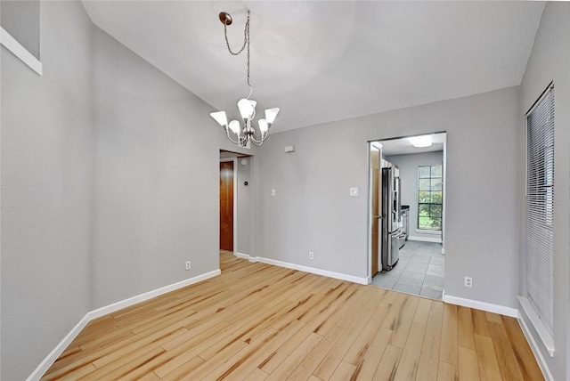 empty room featuring an inviting chandelier, light wood-style flooring, and baseboards