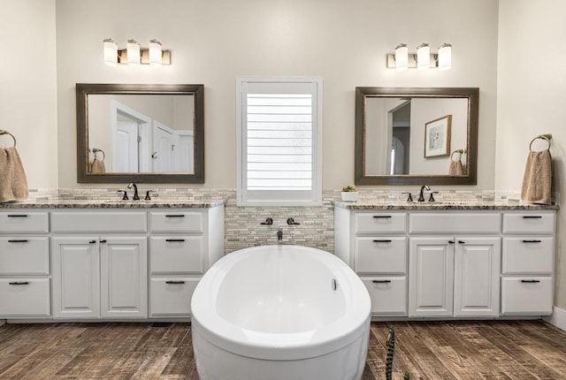 full bathroom featuring a soaking tub, two vanities, a sink, and wood finished floors