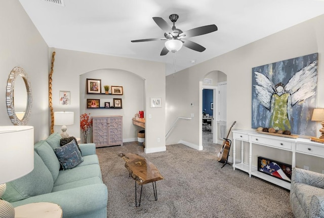 living area featuring baseboards, ceiling fan, arched walkways, and carpet flooring