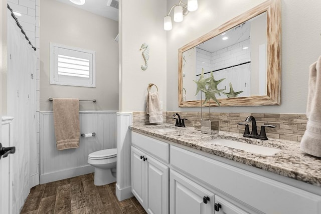 full bathroom with double vanity, wainscoting, toilet, wood finished floors, and a sink