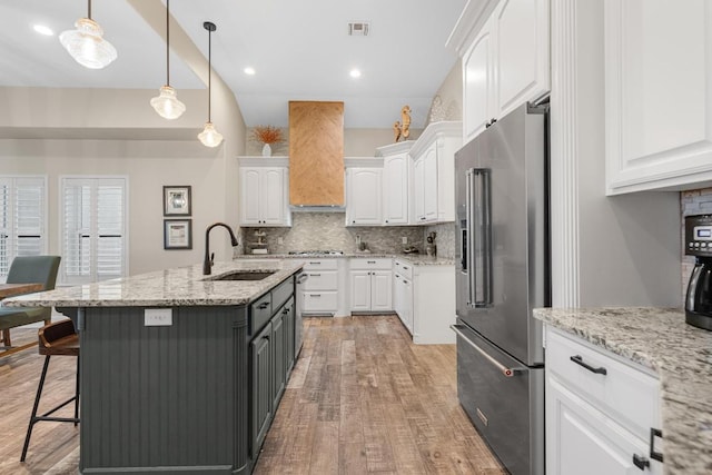 kitchen featuring high end refrigerator, visible vents, white cabinets, premium range hood, and a sink