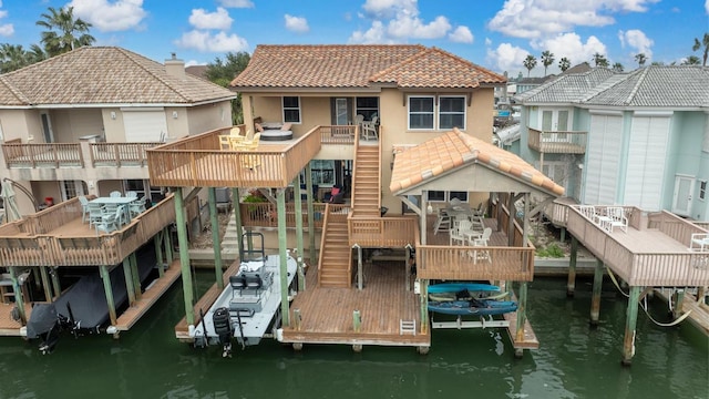 back of property with boat lift, stucco siding, a deck with water view, a tiled roof, and stairs